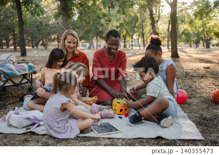 Diverse group of preschoolers playing with teachers in the park Diverse group of preschoolers playing with teachers in the park 140355473