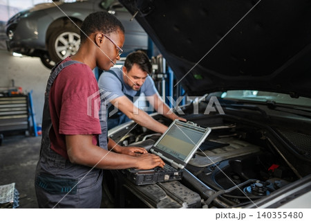 Mechanics using diagnostic software on laptop are examining car engine 140355480
