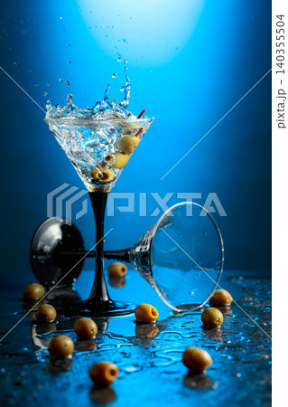 Green olives and glass of martini on a black stone table. Green olives and glass of martini on a black stone table. 140355504