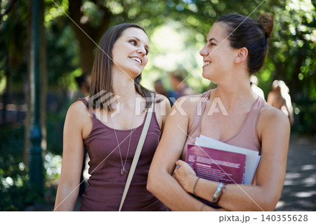 Students, friends and talking of education on campus with learning, knowledge and books at college. Happy women with outdoor conversation in a park or university for scholarship, study or opportunity 140355628