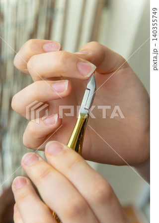 Vertical close up of female hands using cuticle nippers on balcony 140355749
