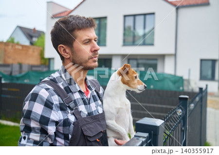 Man holding small dog near metal fence outside modern house. Concept of pet owner lifestyle 140355917