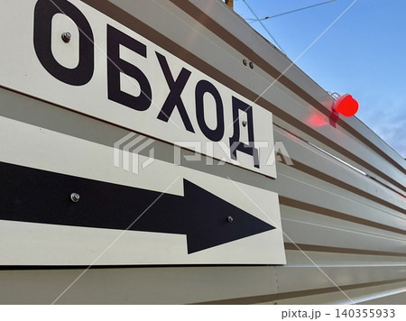 Russian language detour sign on construction fence at evening, safety signage with Cyrillic text, work zone navigation concept 140355933