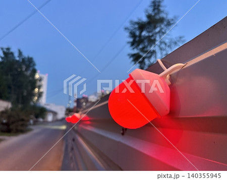 Close-up red warning light glowing on construction fence at night, blurred industrial background with bokeh, work zone safety concept 140355945