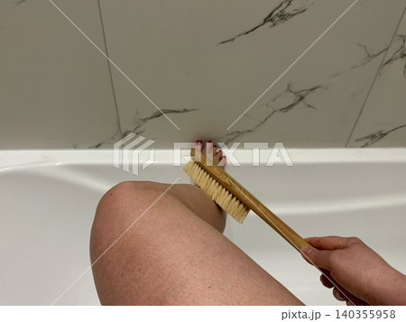 Close-up female hand holding body brush near leg in bathroom, self-care skincare routine and wellness concept at home Close-up female hand holding body brush near leg in bathroom, self-care skincare routine and wellness concept at home 140355958