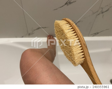 Close-up female hand holding body brush near leg in bathroom, self-care skincare routine and wellness concept at home Close-up female hand holding body brush near leg in bathroom, self-care skincare routine and wellness concept at home 140355961
