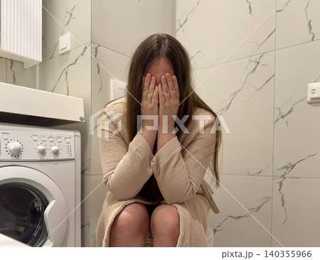Woman in bathrobe sitting on bathroom with face in hands, messy hair, emotional burnout and psychological crisis concept Woman in bathrobe sitting on bathroom with face in hands, messy hair, emotional burnout and psychological crisis concept 140355966