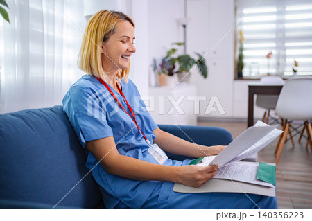 Smiling nurse reviewing medical records at home 140356223