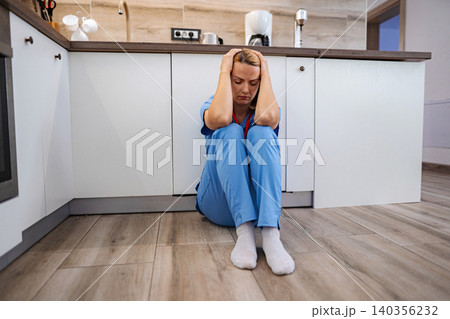 Exhausted doctor sitting on the floor in the kitchen after work 140356232