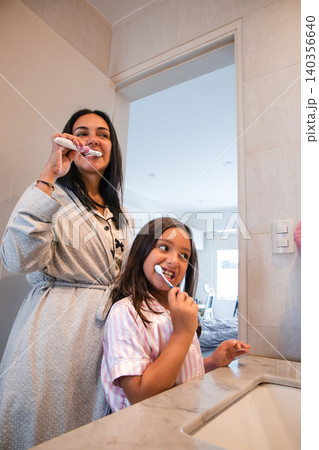 A woman and a girl are brushing their teeth in a bathroom A woman and a girl are brushing their teeth in a bathroom 140356640