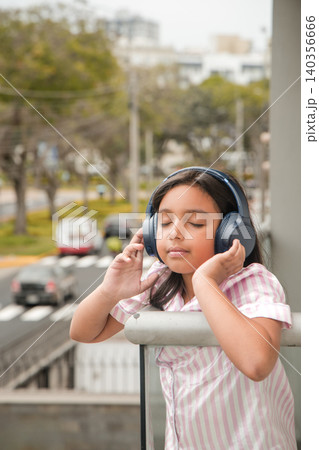 A girl wearing headphones is sitting on a railing A girl wearing headphones is sitting on a railing 140356666
