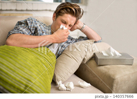 Virus, influenza or man sneezing into tissue on sofa with cold, bug or hay fever at home. Flu, allergies or person with toilet paper for viral infection, bacteria or coughing with sinusitis in house Virus, influenza or man sneezing into tissue on sofa with cold, bug or hay fever at home. Flu, allergies or person with toilet paper for viral infection, bacteria or coughing with sinusitis in house 140357666