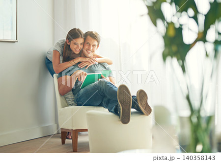 Couple, embrace and book in home, love and chair to relax in lounge on sofa for learning. Man, woman and romance while happy, smile and reading for entertainment and together in living room with hug Couple, embrace and book in home, love and chair to relax in lounge on sofa for learning. Man, woman and romance while happy, smile and reading for entertainment and together in living room with hug 140358143
