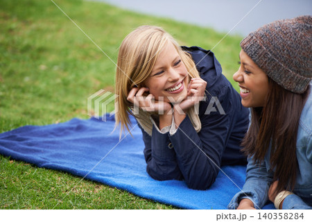 Happy, friends and relax on blanket for picnic outdoor in summer on holiday or vacation together. Women, smile and laugh in conversation in park, woods or lying on grass in backyard or garden 140358284