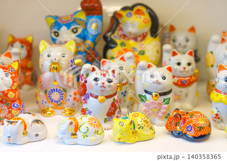 Kanazawa, Japan - Oct 6 2024, A close-up view of white cat and maneki-neko figurines decorated with various colorful flower and dot patterns on a shelf in a souvenir shop of Kanazawa, Japan 140358365