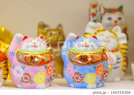Kanazawa, Japan - Oct 6 2024, A close-up view of white cat and maneki-neko figurines decorated with various colorful flower and dot patterns on a shelf in a souvenir shop of Kanazawa, Japan 140358366
