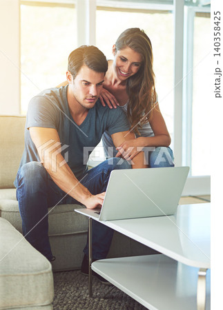 Couple, home and couch with laptop, bonding and entertainment in living room with smile and laugh. Man, woman and sofa with embrace, relax and love while pointing at tech in lounge at house 140358425