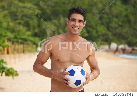 Portrait, soccer ball and body of man on beach in summer for sports, travel or tropical vacation. Exercise, fitness and football with happy young shirtless person on sand for sports on coastal sand Portrait, soccer ball and body of man on beach in summer for sports, travel or tropical vacation. Exercise, fitness and football with happy young shirtless person on sand for sports on coastal sand 140358842