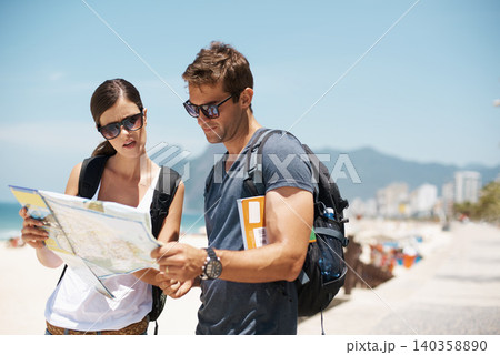 Couple, map and reading with direction at beach, summer and ideas to check path on vacation. Woman, man and chart for location, landmark and travel with search on sidewalk, sea and nature in Italy Couple, map and reading with direction at beach, summer and ideas to check path on vacation. Woman, man and chart for location, landmark and travel with search on sidewalk, sea and nature in Italy 140358890