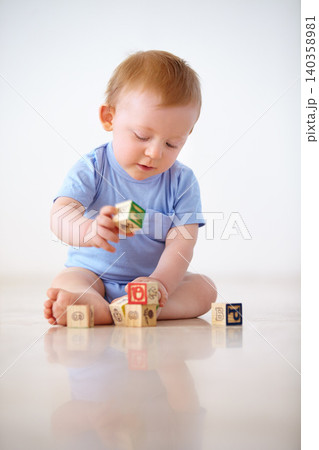 Baby boy, wooden blocks and playing with toys in early childhood development on a gray studio background. Little toddler or child on floor with shape or cube in building, learning or cognitive skills 140358981