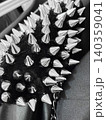 Closeup view of spiked accessory of metal and fabric. Spikes arranged in pattern, with mix textures. Dark background, shiny silver of spikes. Part of fashion accessory or clothing detail 140359041
