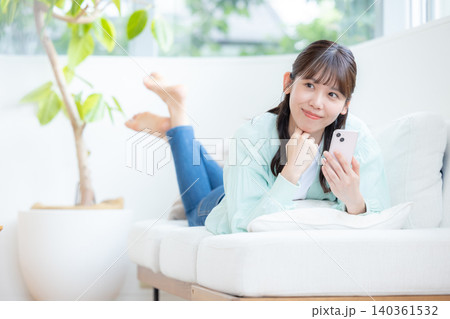 ライフスタイル ソファーに寝そべりスマホを見る女性 ライフスタイル ソファーに寝そべりスマホを見る女性 140361532