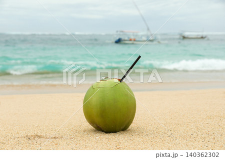 Coconut drink sits on the sand near the water Coconut drink sits on the sand near the water 140362302