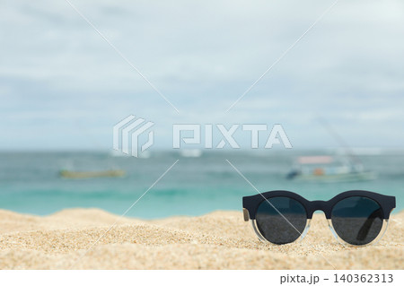 Sunglasses are on sand with ocean and boats in Bali Sunglasses are on sand with ocean and boats in Bali 140362313