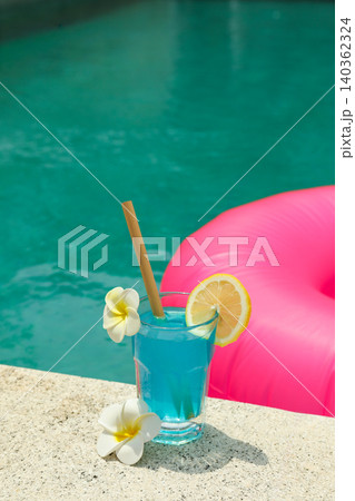 A blue drink with a lemon slice sits by the poolside A blue drink with a lemon slice sits by the poolside 140362324