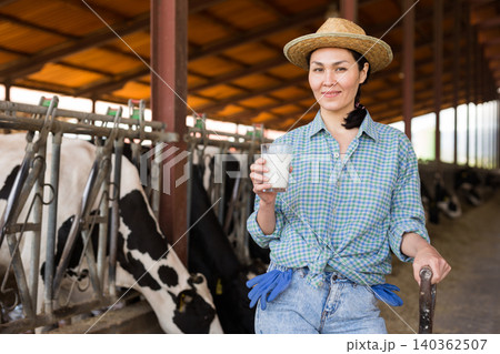 Portrait of a positive kazakh farmer woman in a cowshed, holding a glass of milk 140362507