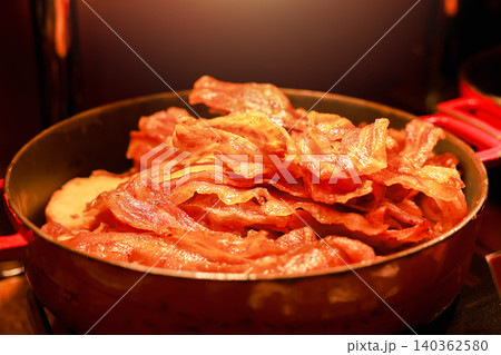 Close up of delicious cooked crispy fried bacon slices piled in a pan at a luxury hotel breakfast buffet. Tasty roasted savory pork meat dish for morning brunch catering under warm lighting. 140362580