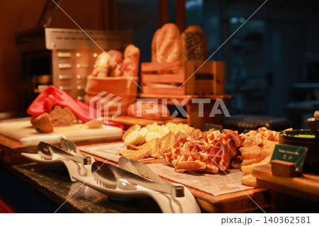 Freshly baked golden waffles, french toast, and rustic bread loaves displayed at a luxury hotel breakfast buffet station. Morning bakery catering setup with serving tongs under warm ambient lighting. 140362581