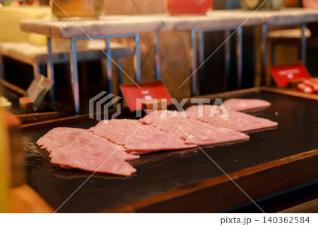 Close up of delicious sliced pork ham folded in triangles arranged on a dark stone platter at a luxury hotel breakfast buffet. Tasty charcuterie cold cuts for morning brunch catering food display. Close up of delicious sliced pork ham folded in triangles arranged on a dark stone platter at a luxury hotel breakfast buffet. Tasty charcuterie cold cuts for morning brunch catering food display. 140362584