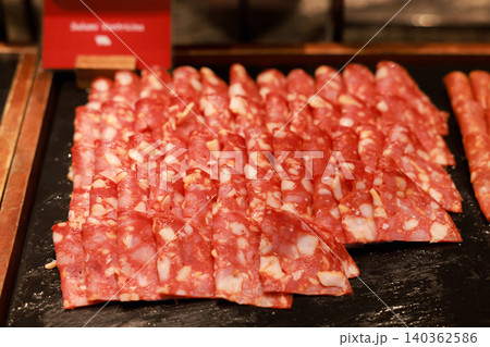 Close up of delicious sliced pork salami cured meat arranged on a dark stone platter at a luxury hotel breakfast buffet. Tasty charcuterie cold cuts for morning brunch catering and food display. Close up of delicious sliced pork salami cured meat arranged on a dark stone platter at a luxury hotel breakfast buffet. Tasty charcuterie cold cuts for morning brunch catering and food display. 140362586