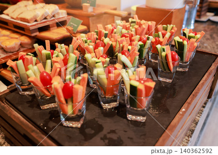 Fresh raw vegetable sticks of carrot and cucumber with cherry tomatoes served in small glass cups on a tray at a hotel breakfast buffet. Healthy vegan diet appetizer snack catering event display. Fresh raw vegetable sticks of carrot and cucumber with cherry tomatoes served in small glass cups on a tray at a hotel breakfast buffet. Healthy vegan diet appetizer snack catering event display. 140362592
