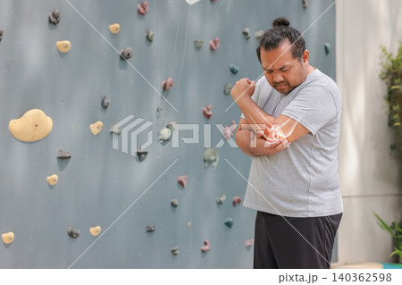Overweight Asian man suffering from elbow joint pain with glowing bone anatomy graphic overlay after rock climbing exercise. Sports injury, arthritis and muscle inflammation medical healthcare concept Overweight Asian man suffering from elbow joint pain with glowing bone anatomy graphic overlay after rock climbing exercise. Sports injury, arthritis and muscle inflammation medical healthcare concept 140362598