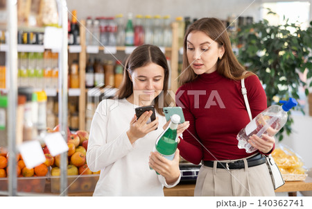 Teenage girl and her mother scanning QR on bottle of soda in supermarket Teenage girl and her mother scanning QR on bottle of soda in supermarket 140362741