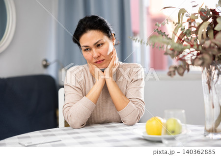 Depressed Asian woman sitting at table Depressed Asian woman sitting at table 140362885