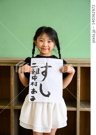 教室の後ろで笑顔で「すし」の習字作品を見せる女子小学生 140362972