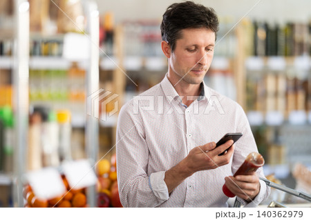 Man in light shirt scan QR code and take reading ketchup label using phone camera in shop Man in light shirt scan QR code and take reading ketchup label using phone camera in shop 140362979