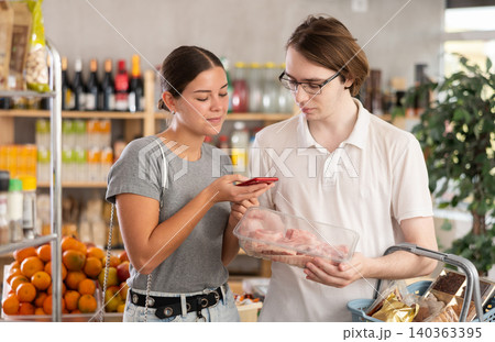In shop youth spouses scan QR code and take reading raw pork tenderloin package using phone camera In shop youth spouses scan QR code and take reading raw pork tenderloin package using phone camera 140363395