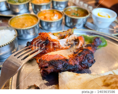 インドカレー店で食べるタンドリーチキンのクローズアップ。フォークで食べる様子。カレーを背景に。 140363586