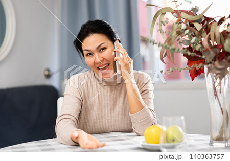 Happy woman talking on phone while sitting at table at home 140363757
