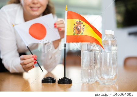 Little flag of Spain on table and flag of Japan put next to it by young woman Little flag of Spain on table and flag of Japan put next to it by young woman 140364003