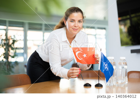 Employee of delegation prepares negotiating table - sets up flag of NATO (OTAN) and Turkey Employee of delegation prepares negotiating table - sets up flag of NATO (OTAN) and Turkey 140364012