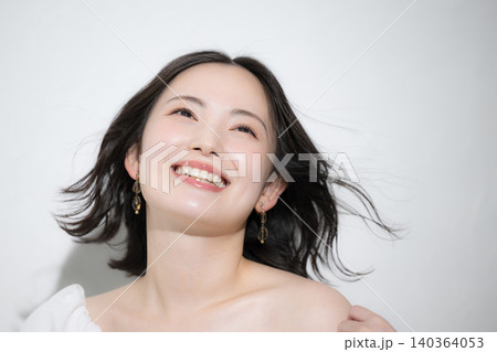 風になびく髪と透明感のある笑顔が美しい若い女性のスキンケアやヘアケアビューティーイメージ見上げる 140364053