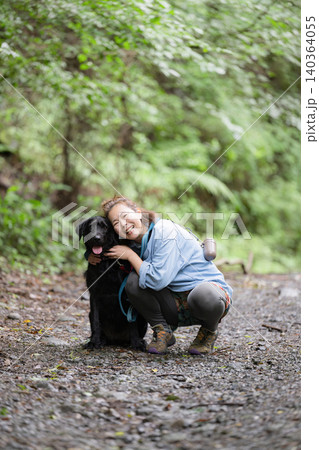 森の中で愛犬と触れ合いながら笑顔を見せる女性のアウトドアライフカメラ目線 140364055