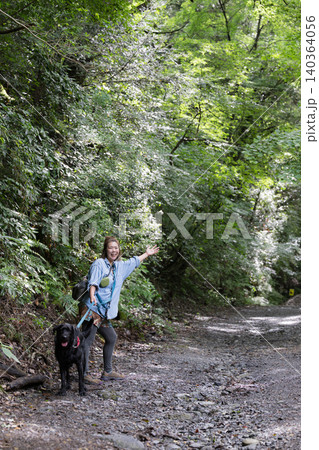 森の中で愛犬と触れ合いながら笑顔を見せる女性のアウトドアライフカメラ目線 森の中で愛犬と触れ合いながら笑顔を見せる女性のアウトドアライフカメラ目線 140364056