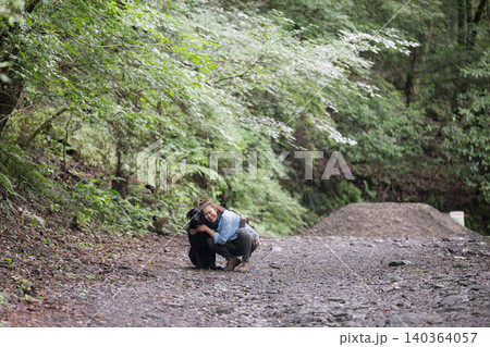 森の中で愛犬と触れ合いながら笑顔を見せる女性のアウトドアライフカメラ目線 森の中で愛犬と触れ合いながら笑顔を見せる女性のアウトドアライフカメラ目線 140364057