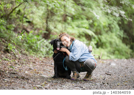 森の中で愛犬と触れ合いながら笑顔を見せる女性のアウトドアライフカメラ目線 森の中で愛犬と触れ合いながら笑顔を見せる女性のアウトドアライフカメラ目線 140364059